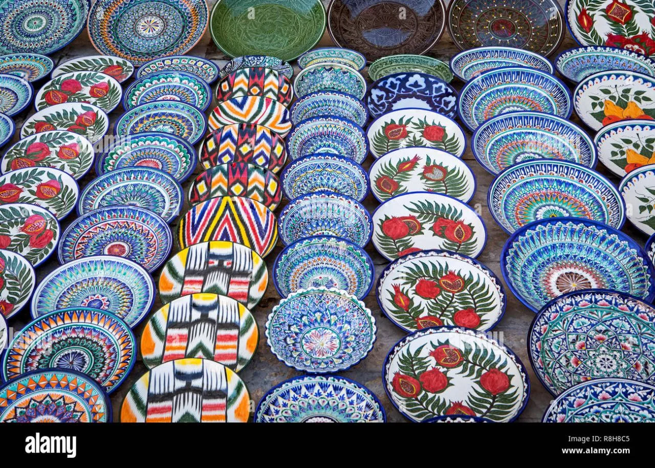 Tourists visiting a traditional Gijduvan pottery workshop in Samarkand, sitting among hand-painted Uzbek ceramics while a local artisan demonstrates pottery making